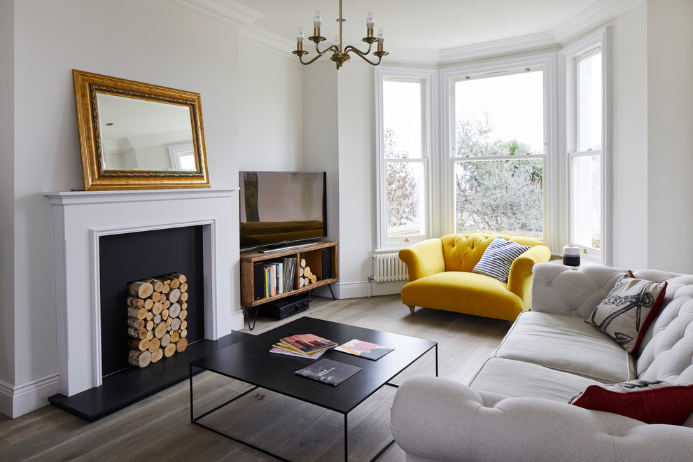 This is an example of a medium sized modern enclosed living room in London with white walls, light hardwood flooring, a standard fireplace, a metal fireplace surround, a freestanding tv and brown floors.