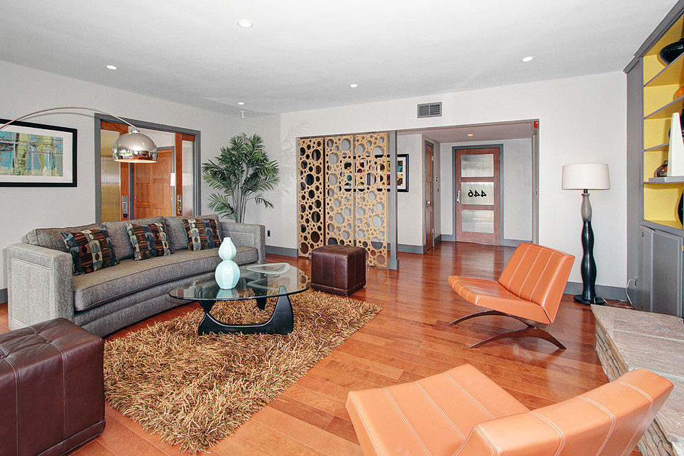 Mid-century modern medium tone wood floor and brown floor living room photo in Los Angeles with white walls, a standard fireplace, a stone fireplace and no tv