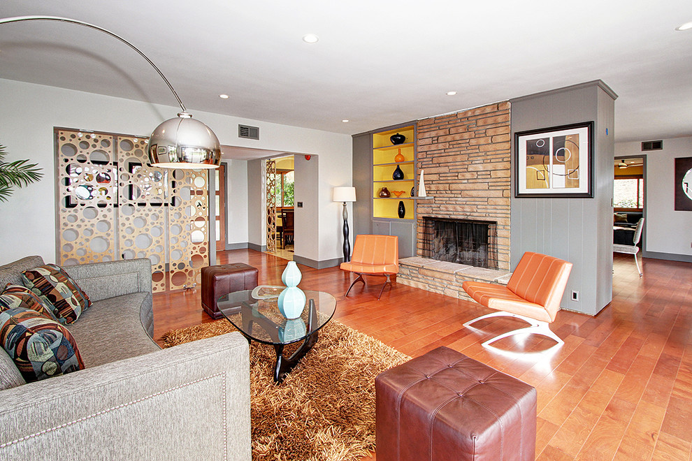 Réalisation d'un salon vintage ouvert avec un mur gris, un sol en bois brun, une cheminée standard et un manteau de cheminée en pierre.