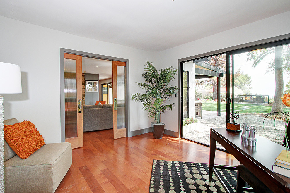 Offenes Retro Wohnzimmer mit grauer Wandfarbe, braunem Holzboden, Kamin und Kaminumrandung aus Stein in Los Angeles