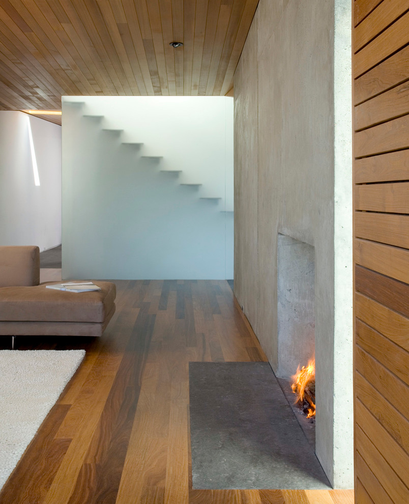 Источник вдохновения для домашнего уюта: открытая гостиная комната среднего размера в стиле модернизм с серыми стенами, паркетным полом среднего тона, стандартным камином и фасадом камина из бетона