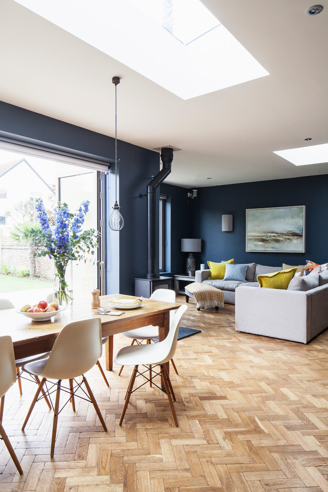 Aménagement d'un grand salon classique ouvert avec un mur bleu, parquet clair, un poêle à bois, un manteau de cheminée en carrelage, un sol marron et un plafond voûté.