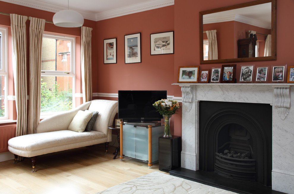 ロンドンにあるお手頃価格の中くらいなトラディショナルスタイルのおしゃれなリビング (オレンジの壁、淡色無垢フローリング、標準型暖炉、石材の暖炉まわり、据え置き型テレビ) の写真