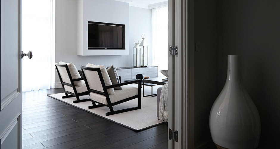 Стильный дизайн: гостиная комната в современном стиле с белыми стенами, темным паркетным полом и телевизором на стене без камина - последний тренд