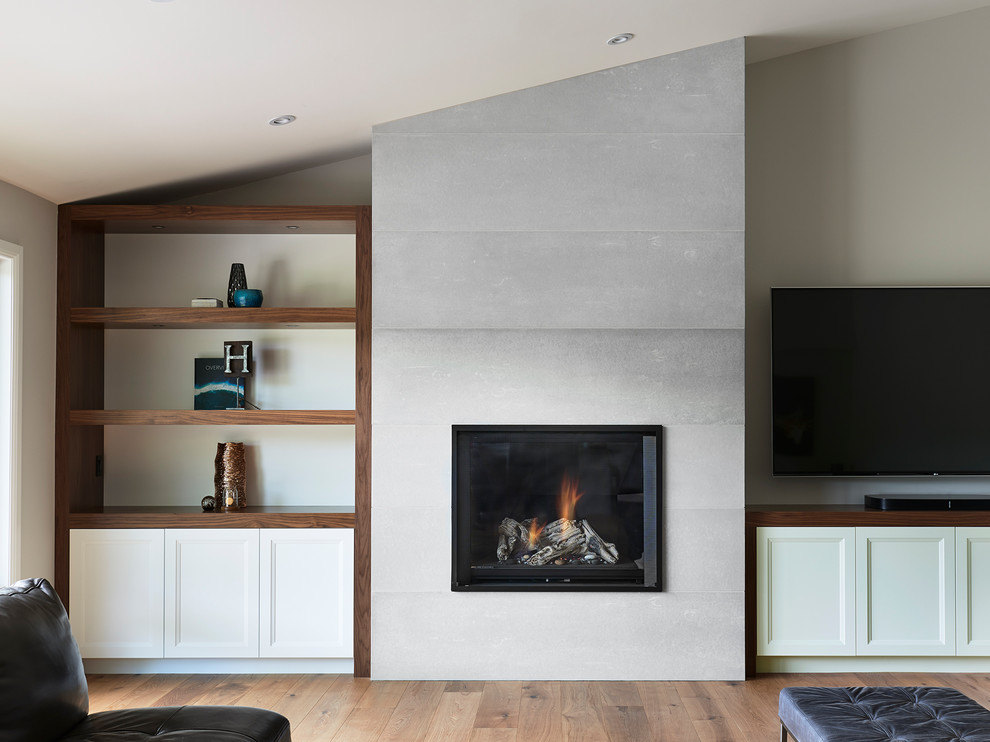 Réalisation d'un salon design de taille moyenne et ouvert avec un mur gris, un sol en bois brun, une cheminée standard, un manteau de cheminée en béton, un téléviseur indépendant et un sol marron.