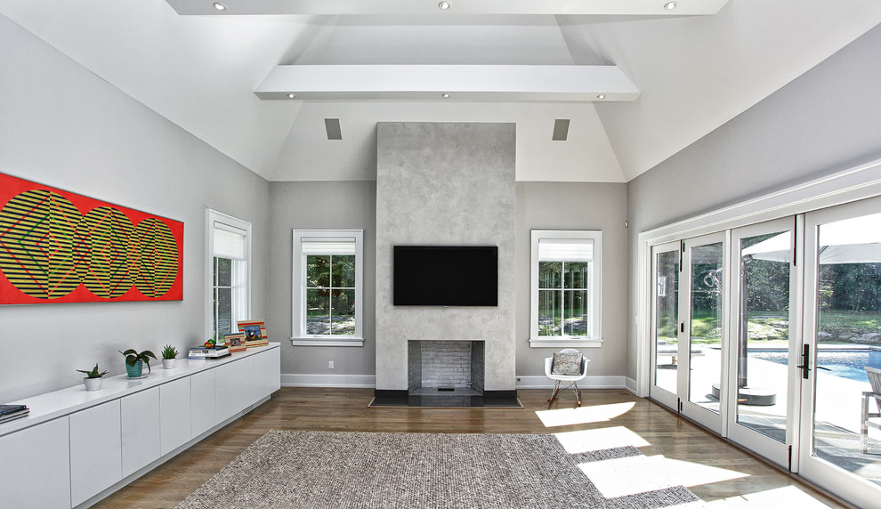Cette image montre un grand salon minimaliste fermé avec un mur gris, un sol en bois brun, une cheminée standard, un manteau de cheminée en béton, un téléviseur fixé au mur et un sol marron.