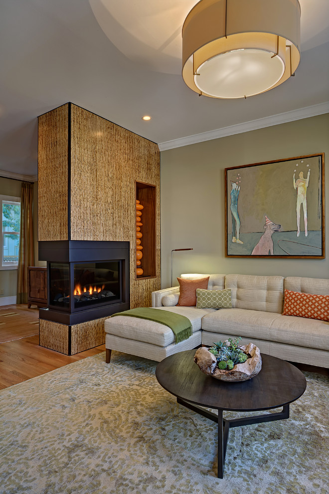 サンフランシスコにある中くらいなミッドセンチュリースタイルのおしゃれなリビング (緑の壁、無垢フローリング、両方向型暖炉、木材の暖炉まわり、テレビなし、茶色い床) の写真