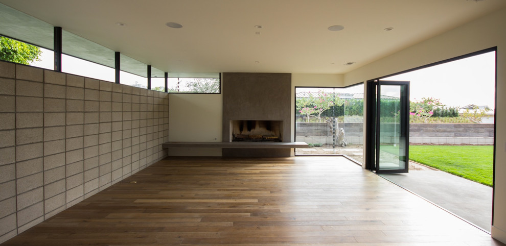 Mittelgroßes, Repräsentatives, Offenes Retro Wohnzimmer mit grauer Wandfarbe, braunem Holzboden, Gaskamin, Kaminumrandung aus Beton und braunem Boden in Los Angeles