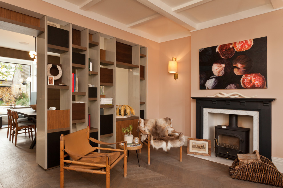 Inspiration pour un salon design de taille moyenne et fermé avec une bibliothèque ou un coin lecture, un mur rose, parquet clair, une cheminée standard et un manteau de cheminée en pierre.