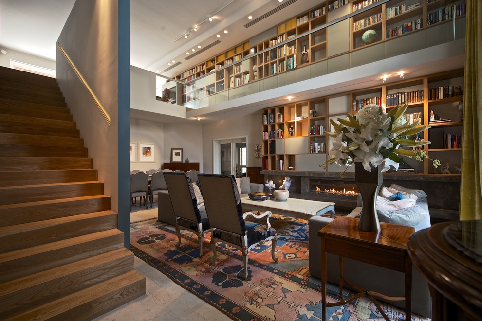 Идея дизайна: большая двухуровневая гостиная комната в современном стиле с с книжными шкафами и полками, серыми стенами, мраморным полом, горизонтальным камином и фасадом камина из камня без телевизора
