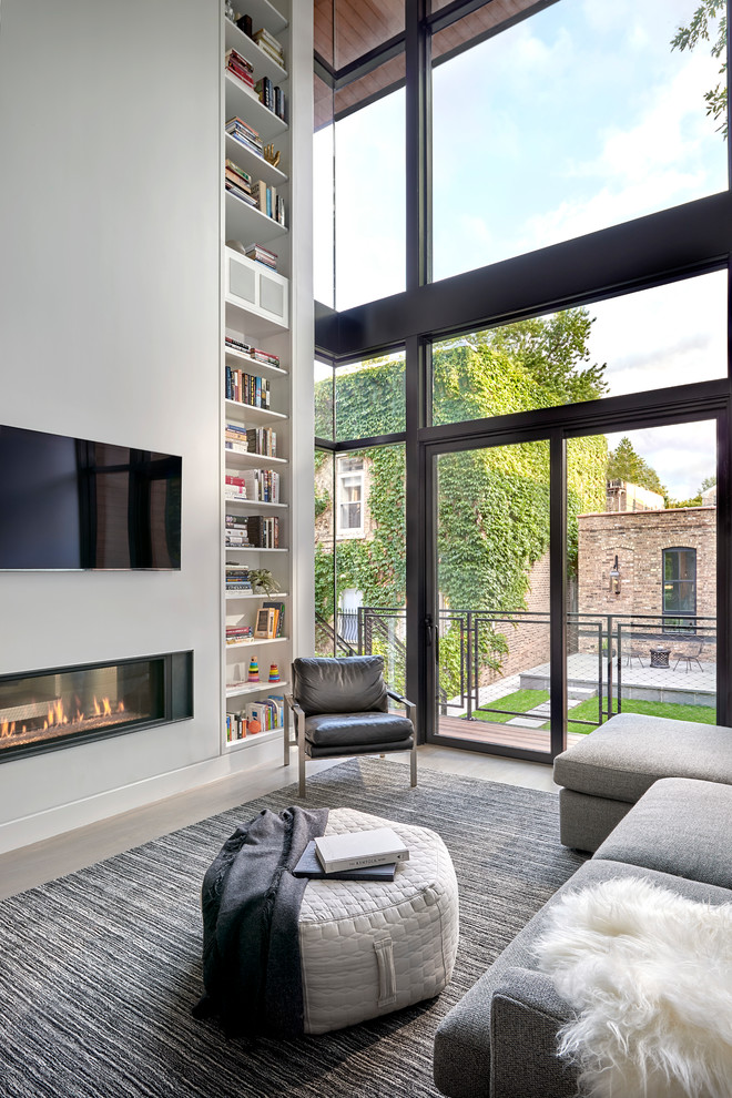 Cette image montre un grand salon mansardé ou avec mezzanine design avec un mur blanc, un sol en bois brun, une cheminée double-face et un téléviseur fixé au mur.