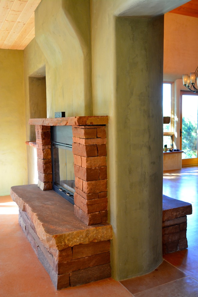 Réalisation d'un salon sud-ouest américain avec un mur vert, sol en béton ciré, une cheminée double-face et un manteau de cheminée en pierre.