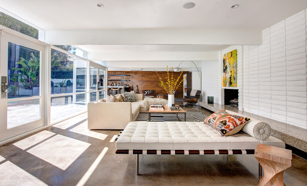 Photo of a large contemporary open plan living room in Orange County with white walls, concrete flooring, a standard fireplace, a brick fireplace surround, no tv, brown floors and feature lighting.