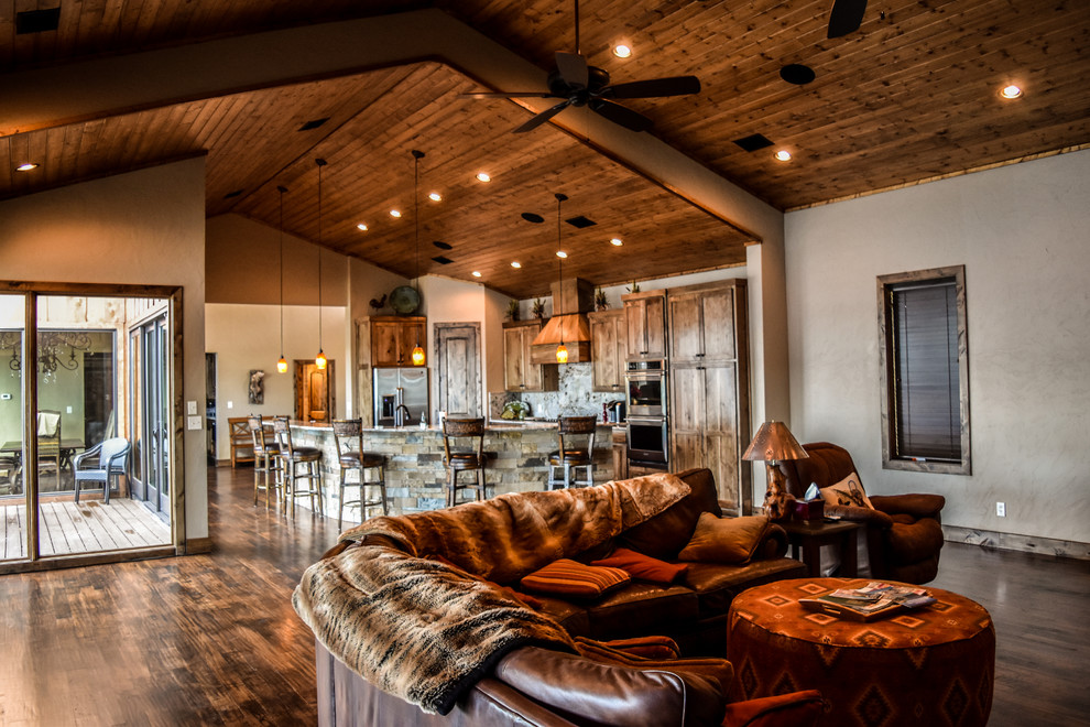 Imagen de salón abierto de estilo americano grande con paredes beige, suelo de madera oscura, suelo marrón, chimenea lineal y marco de chimenea de piedra