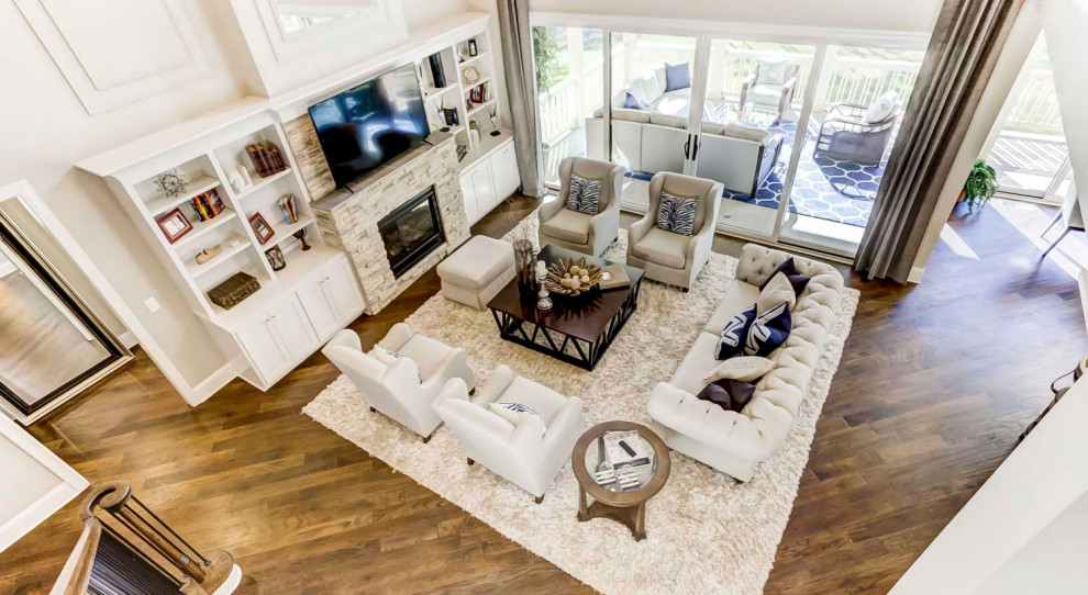 Cette image montre un très grand salon ouvert avec un mur blanc, un sol en bois brun, une cheminée standard, un manteau de cheminée en pierre de parement, un téléviseur encastré, poutres apparentes et du lambris.