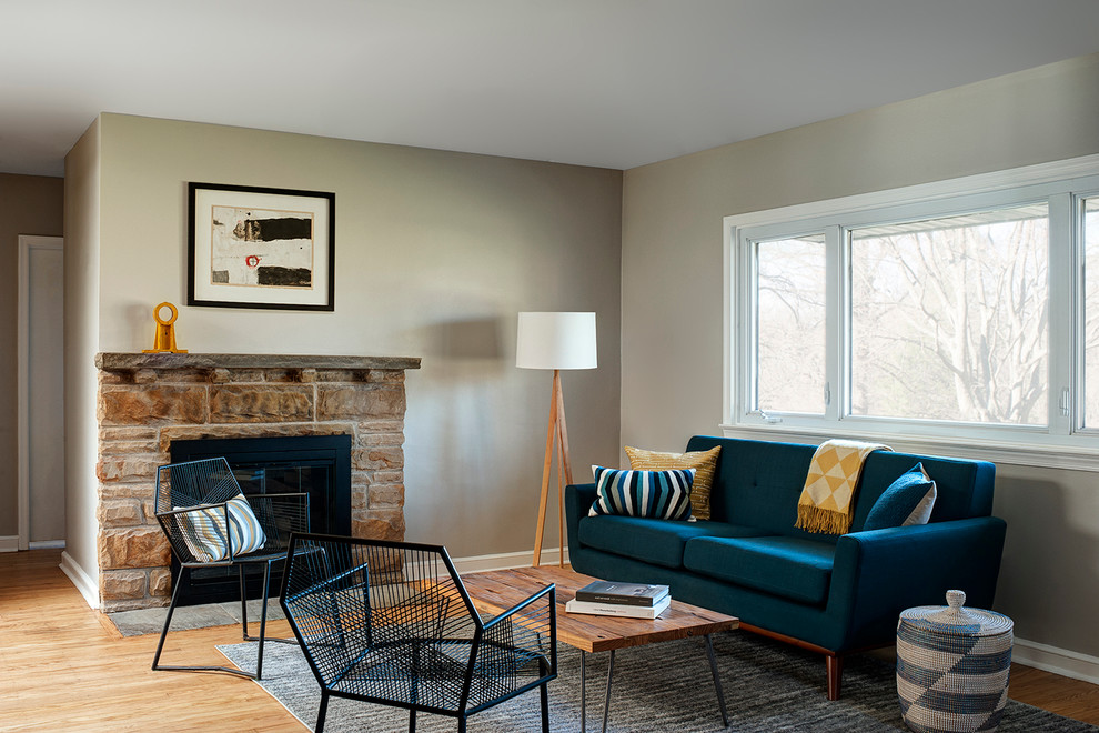 На фото: открытая гостиная комната среднего размера в стиле ретро с серыми стенами, светлым паркетным полом, стандартным камином, фасадом камина из камня и синим диваном без телевизора