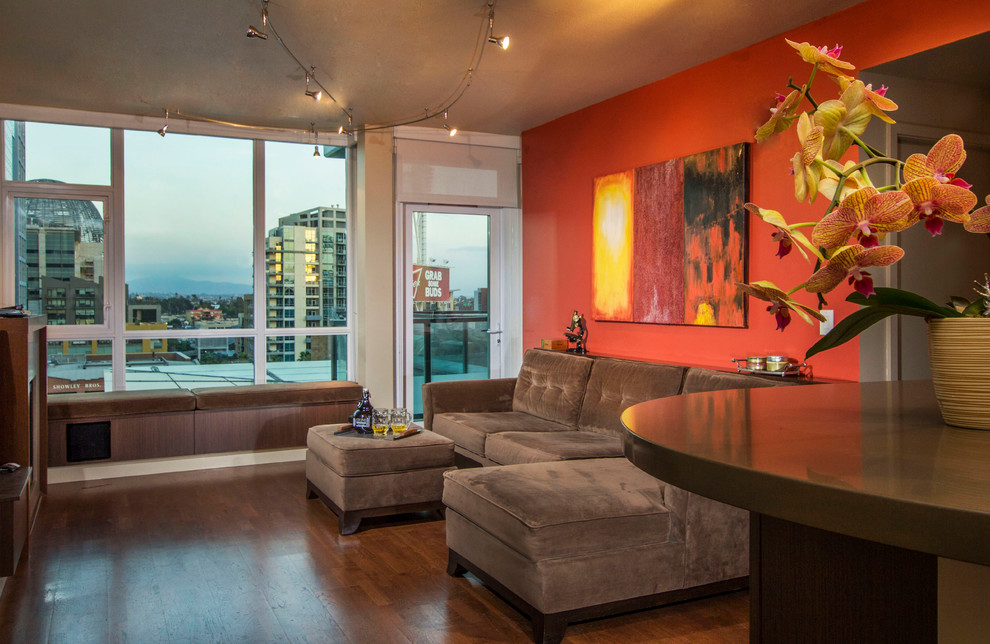 Kleines, Offenes Modernes Wohnzimmer mit oranger Wandfarbe, braunem Holzboden, Kamin, Kaminumrandung aus Stein und TV-Wand in San Diego