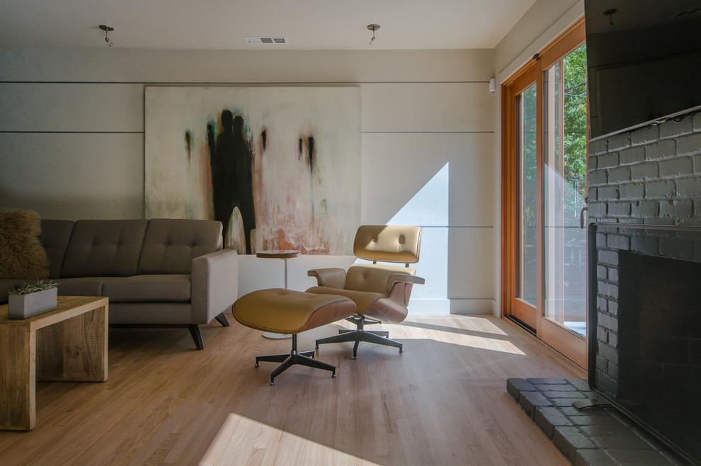 Immagine di un piccolo soggiorno moderno aperto con sala formale, parquet chiaro, cornice del camino in mattoni, TV a parete e pareti beige