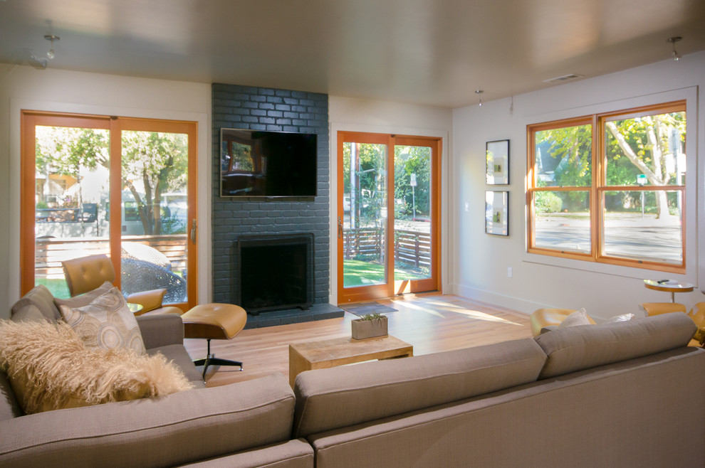 Mittelgroßes, Offenes Modernes Wohnzimmer mit beiger Wandfarbe, hellem Holzboden, Kamin, Kaminumrandung aus Backstein und TV-Wand in Sacramento