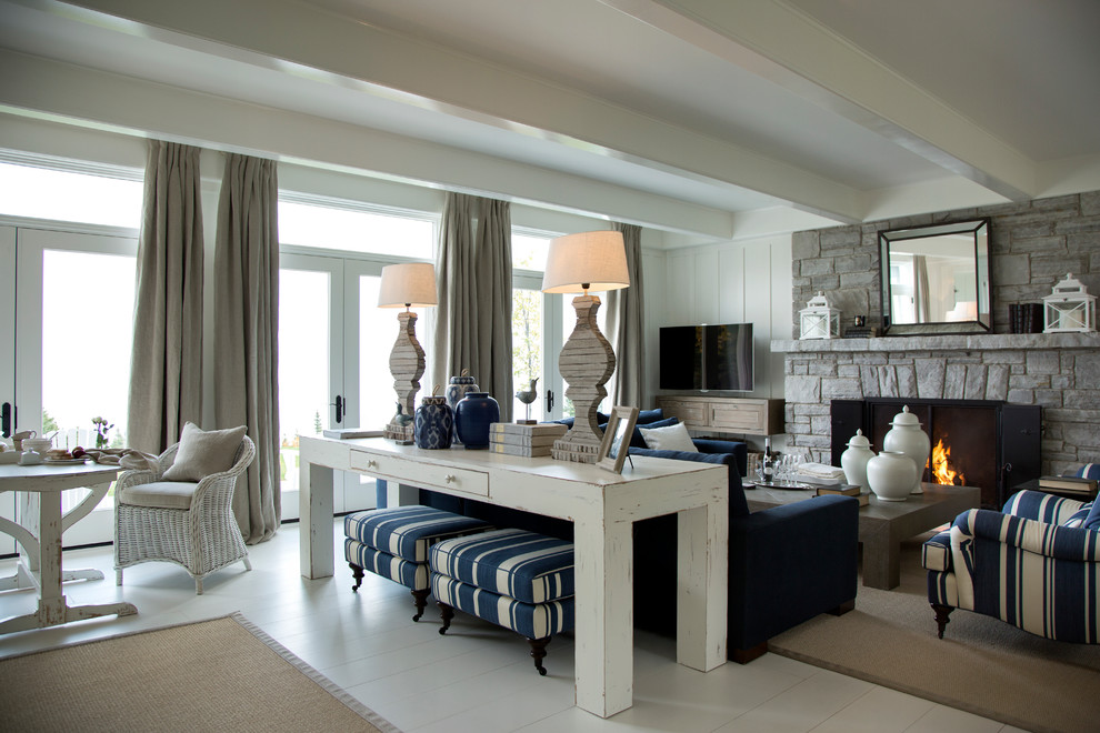На фото: парадная, открытая гостиная комната среднего размера в морском стиле с белыми стенами, деревянным полом, стандартным камином, фасадом камина из камня, телевизором на стене и белым полом с