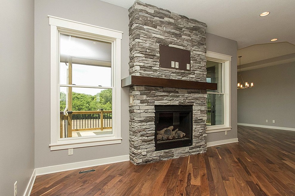 Foto de salón abierto moderno con paredes grises, suelo de madera en tonos medios, todas las chimeneas y marco de chimenea de piedra