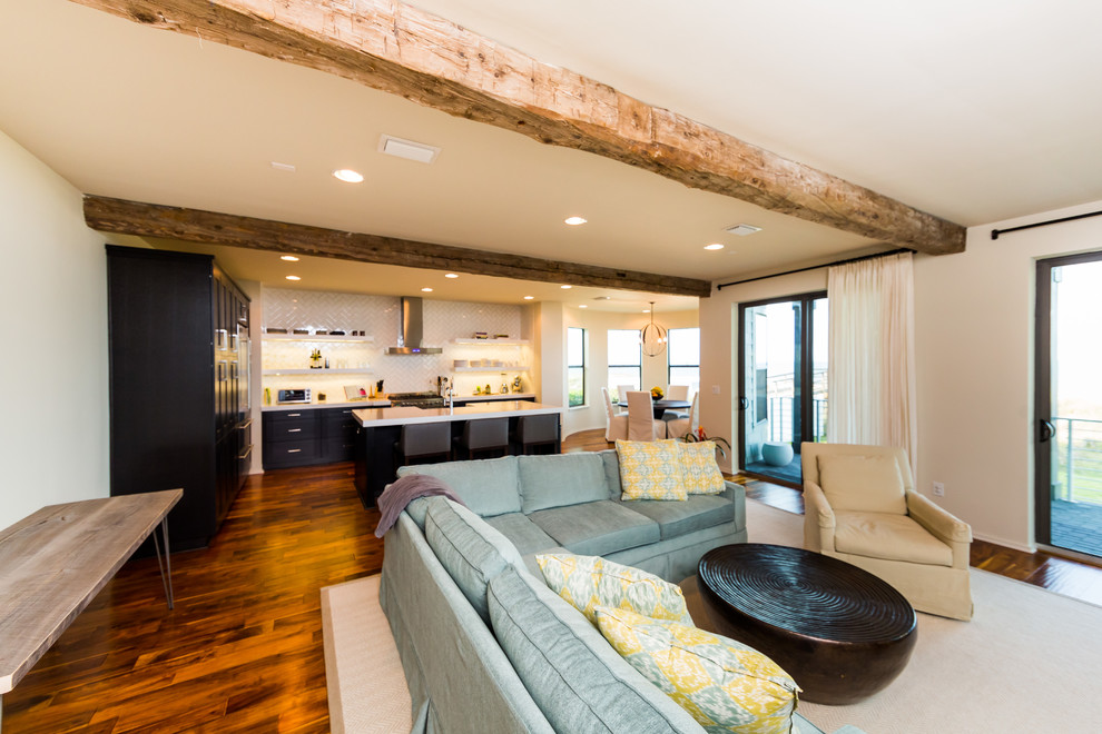 Modelo de salón abierto costero grande con paredes blancas, suelo de madera en tonos medios y televisor colgado en la pared