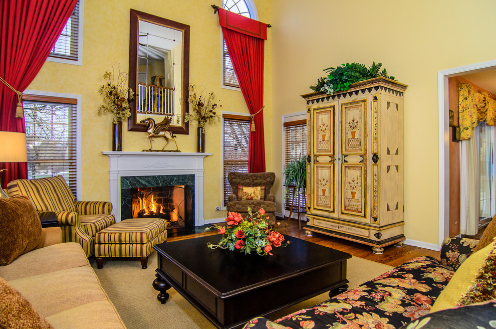 Cette photo montre un grand salon chic ouvert avec une salle de réception, un mur jaune, un sol en bois brun, une cheminée standard, un manteau de cheminée en bois et un téléviseur dissimulé.