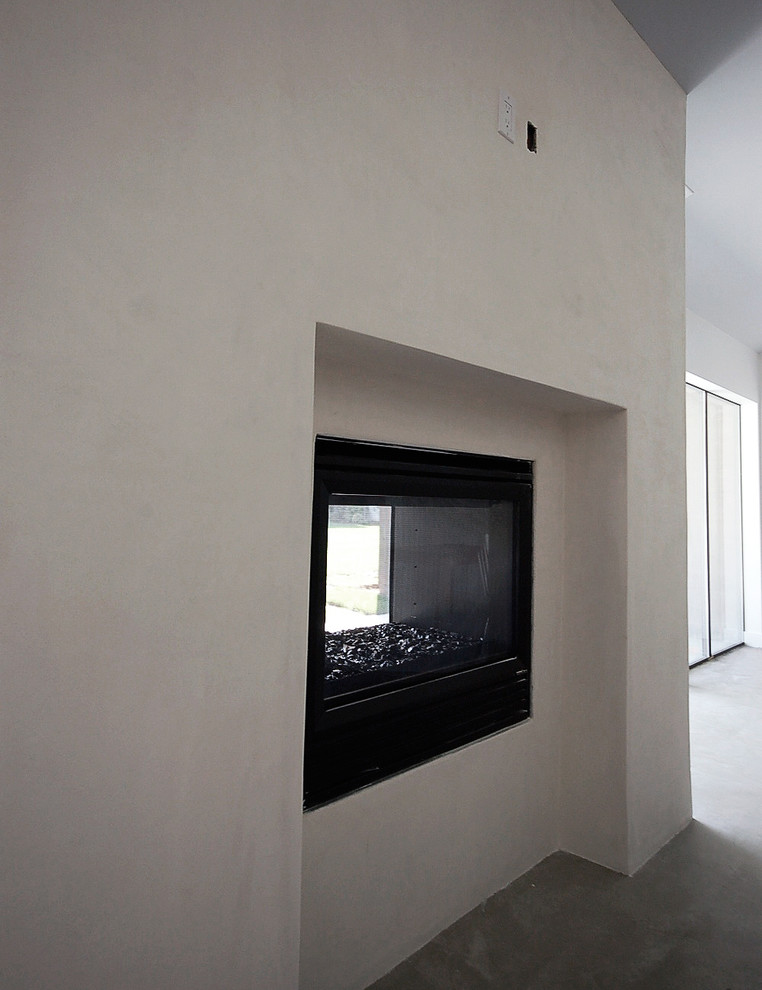 Esempio di un grande soggiorno minimalista aperto con sala formale, pareti bianche, pavimento in cemento, camino bifacciale, cornice del camino in intonaco e TV a parete
