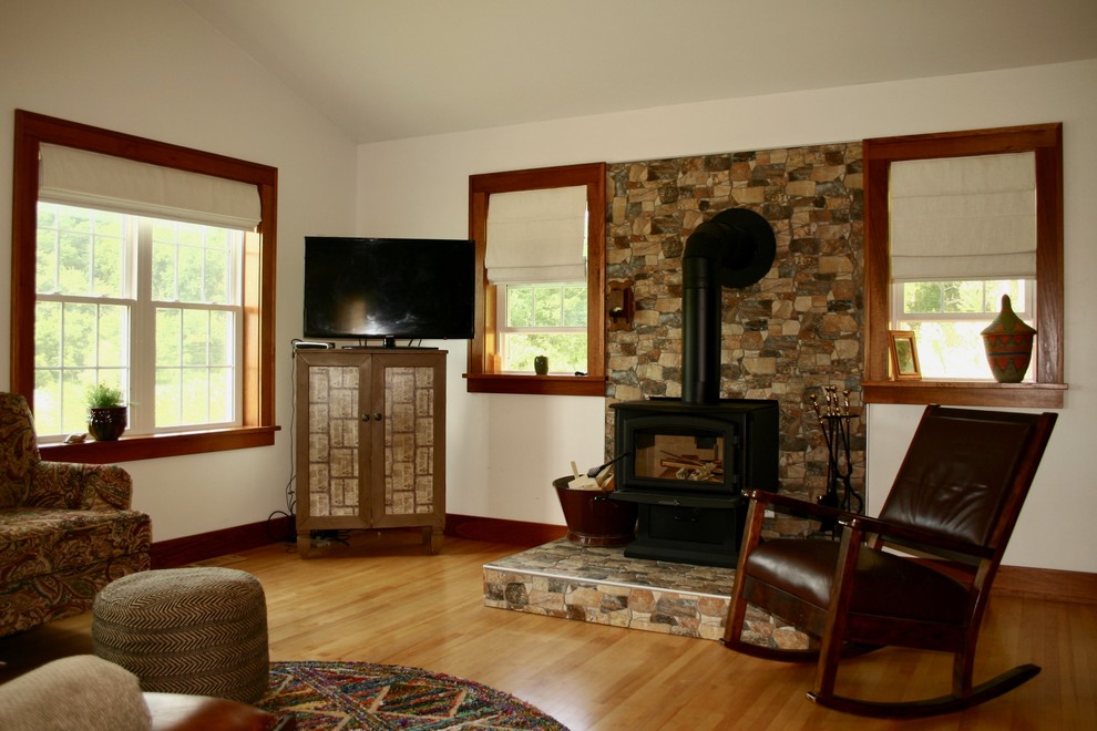 Пример оригинального дизайна: большая изолированная гостиная комната в стиле кантри с белыми стенами, светлым паркетным полом, печью-буржуйкой, фасадом камина из камня и коричневым полом