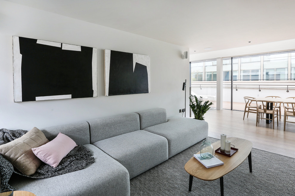 Modelo de salón para visitas abierto contemporáneo pequeño sin chimenea con paredes blancas, suelo de madera clara y televisor retractable