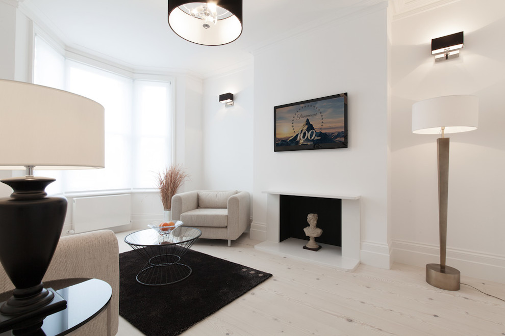 На фото: гостиная комната в скандинавском стиле с белыми стенами, светлым паркетным полом, стандартным камином, телевизором на стене и эркером с