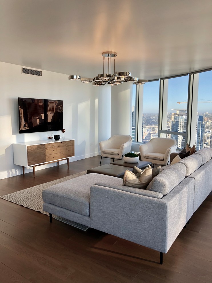 Стильный дизайн: гостиная комната в современном стиле с белыми стенами, темным паркетным полом, телевизором на стене и коричневым полом - последний тренд