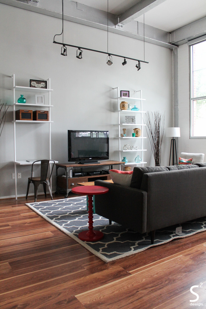 Cette image montre un salon mansardé ou avec mezzanine urbain avec un mur gris, un sol en bois brun et un téléviseur indépendant.