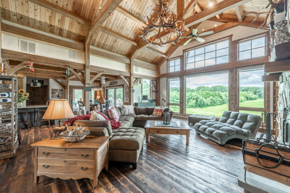 This is an example of a large rustic open plan living room in Milwaukee with beige walls, dark hardwood flooring, a standard fireplace, a stone fireplace surround, a built-in media unit and brown floors.