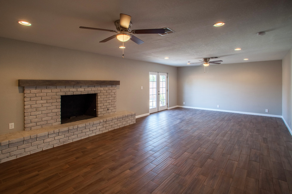 Cette image montre un salon minimaliste de taille moyenne et ouvert avec une salle de réception, un mur beige, un sol en bois brun, une cheminée standard, un manteau de cheminée en brique, aucun téléviseur et un sol marron.