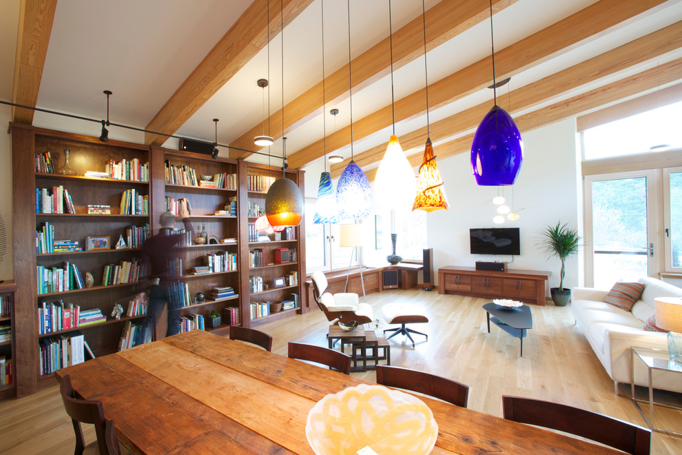 Foto på ett funkis allrum med öppen planlösning, med ett bibliotek, vita väggar, ljust trägolv och en väggmonterad TV