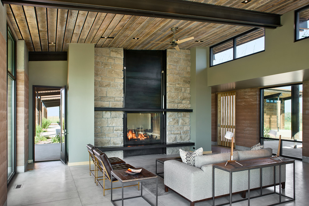 Inspiration pour un salon design avec un mur vert, sol en béton ciré, une cheminée double-face et un manteau de cheminée en pierre.