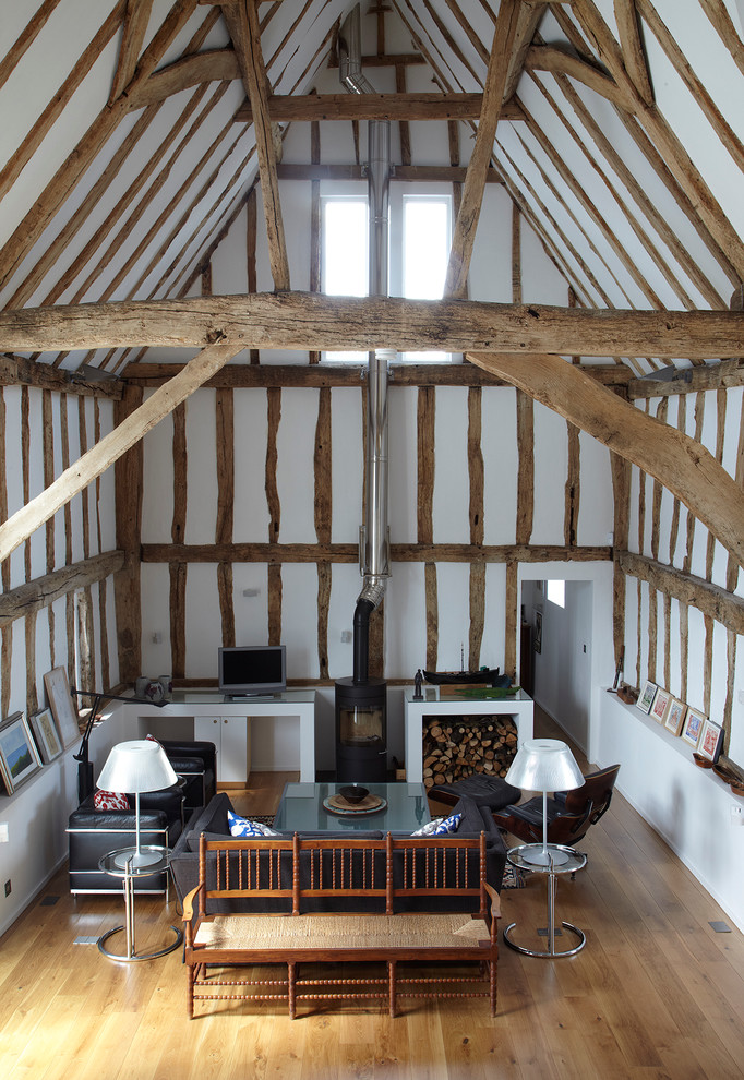 Imagen de salón abierto bohemio de tamaño medio con paredes blancas, suelo de madera clara, televisor independiente y estufa de leña