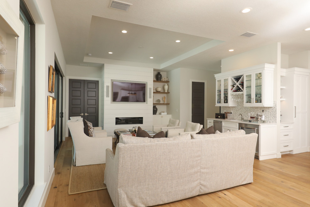 Kleines Maritimes Wohnzimmer mit Hausbar, weißer Wandfarbe, hellem Holzboden, Gaskamin, Kaminumrandung aus Holz und Multimediawand in Tampa