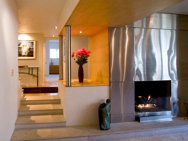Свежая идея для дизайна: двухуровневая гостиная комната в современном стиле с бежевыми стенами, паркетным полом среднего тона, стандартным камином и фасадом камина из металла без телевизора - отличное фото интерьера