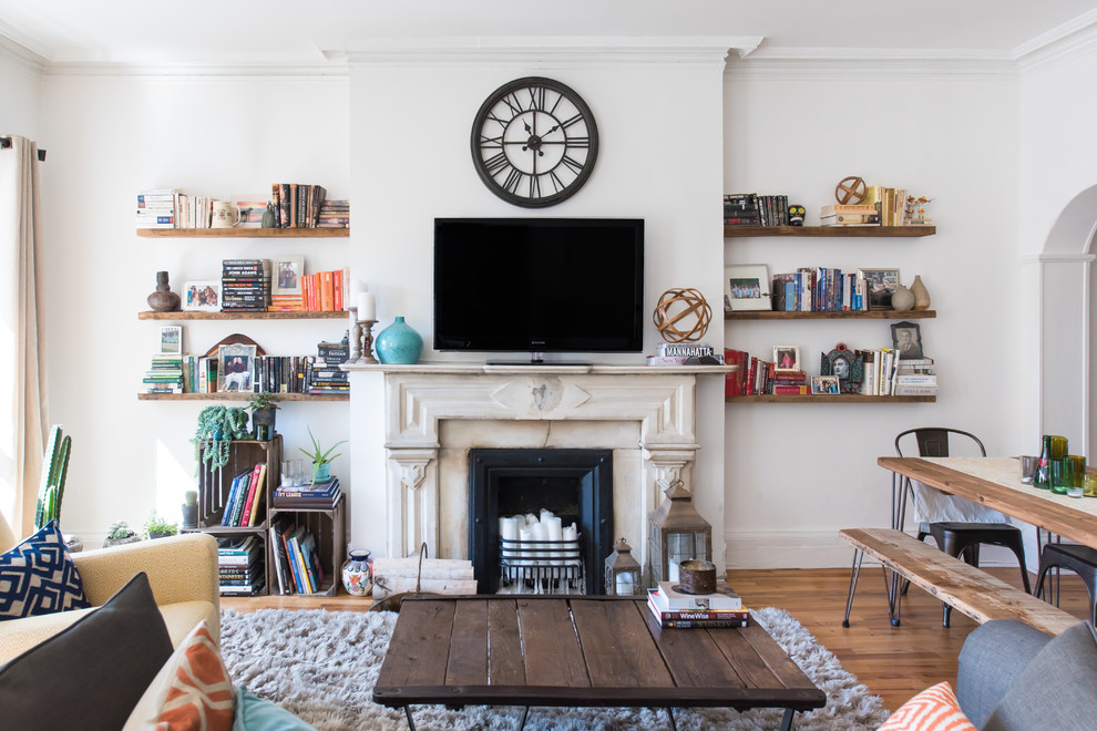 Immagine di un soggiorno boho chic con pareti bianche, pavimento in legno massello medio, camino classico e TV autoportante