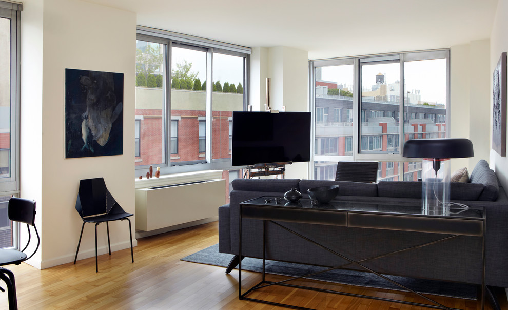 Example of a large minimalist loft-style light wood floor living room design in New York with a bar, white walls and a tv stand