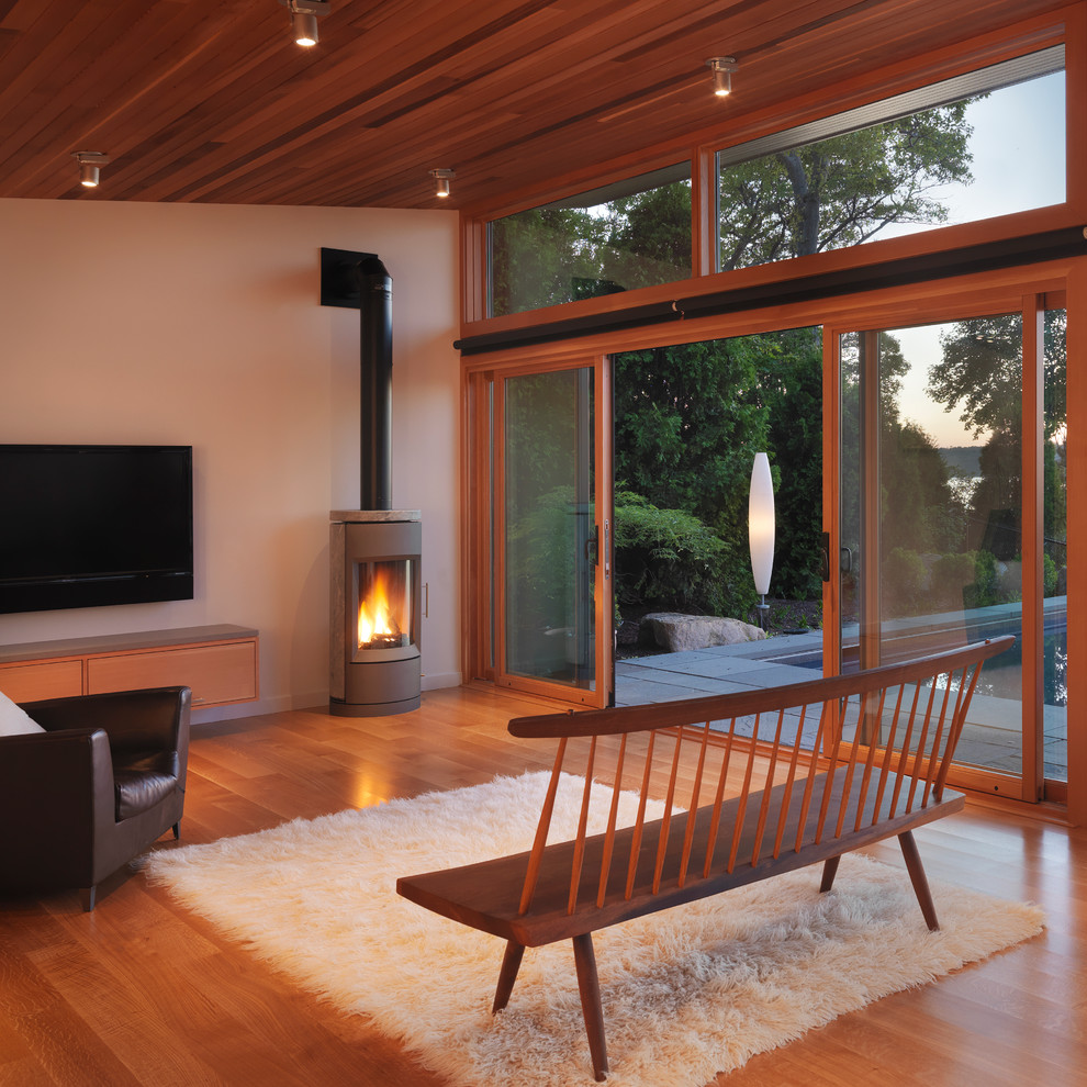 Foto di un piccolo soggiorno minimalista con TV a parete, pareti bianche, pavimento in legno massello medio, cornice del camino in pietra e stufa a legna