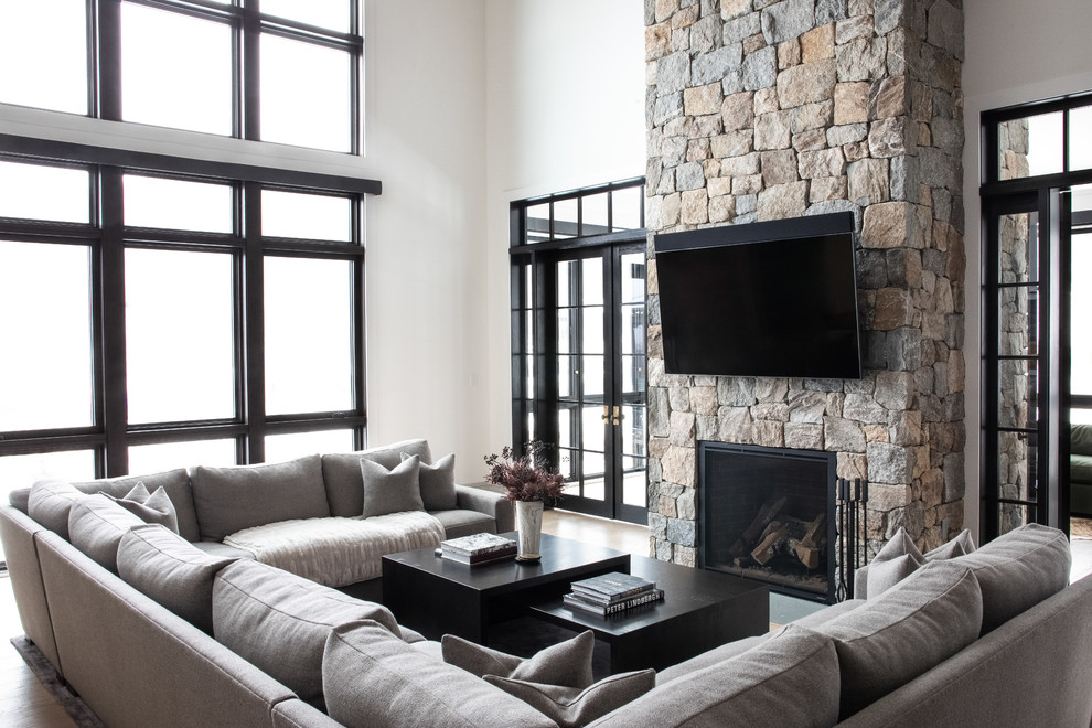 Стильный дизайн: двухуровневая гостиная комната в современном стиле с светлым паркетным полом, стандартным камином и фасадом камина из камня - последний тренд