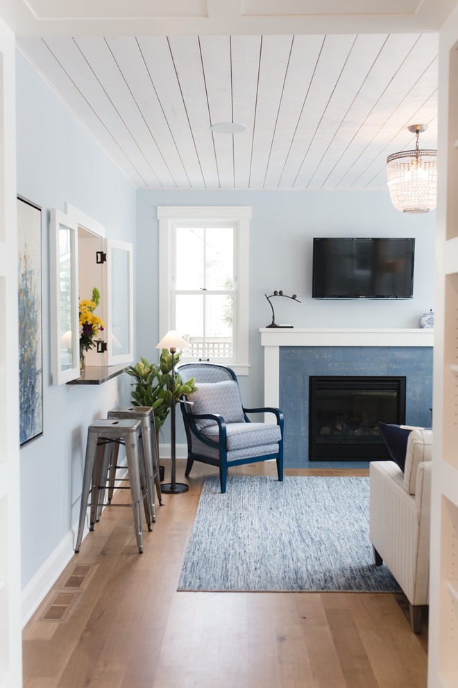 На фото: изолированная гостиная комната среднего размера в стиле кантри с музыкальной комнатой, синими стенами, светлым паркетным полом, стандартным камином, фасадом камина из плитки, телевизором на стене и коричневым полом
