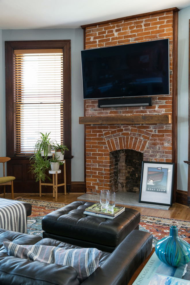 Mid-sized eclectic open concept light wood floor and brown floor living room photo in St Louis with blue walls, a standard fireplace, a brick fireplace and a wall-mounted tv