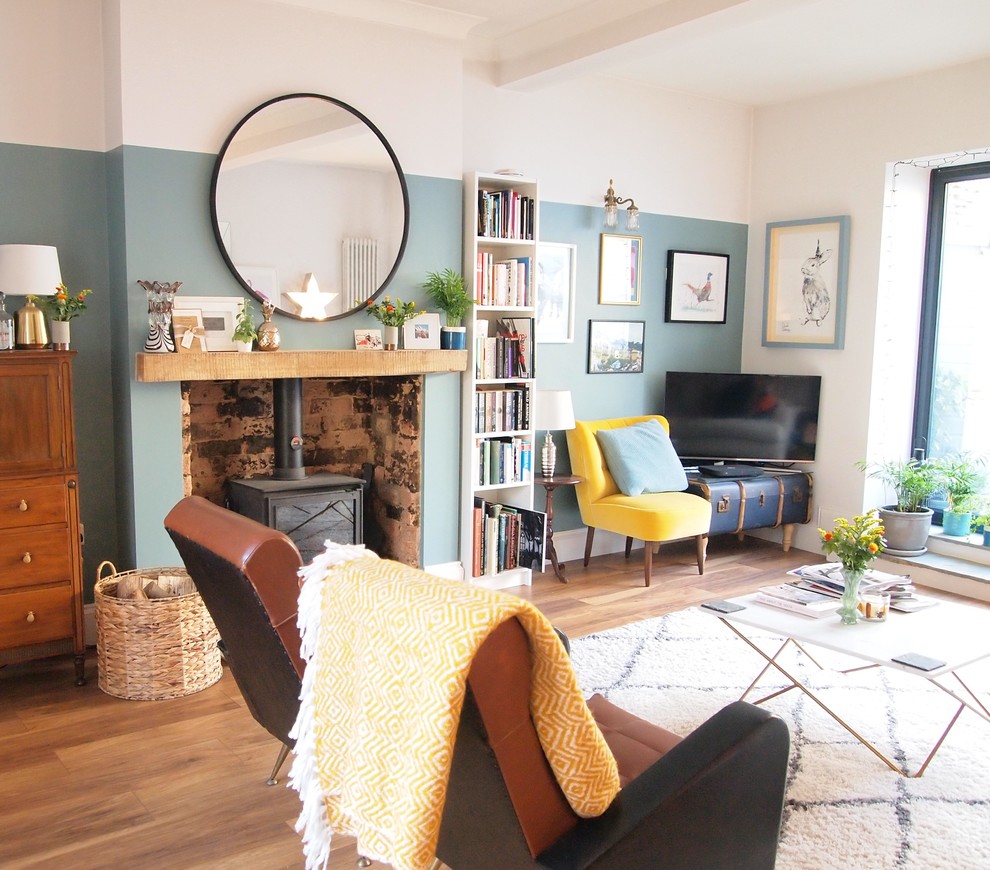 Immagine di un soggiorno eclettico con pareti blu, pavimento in legno massello medio, stufa a legna, cornice del camino in pietra, TV autoportante e pavimento marrone