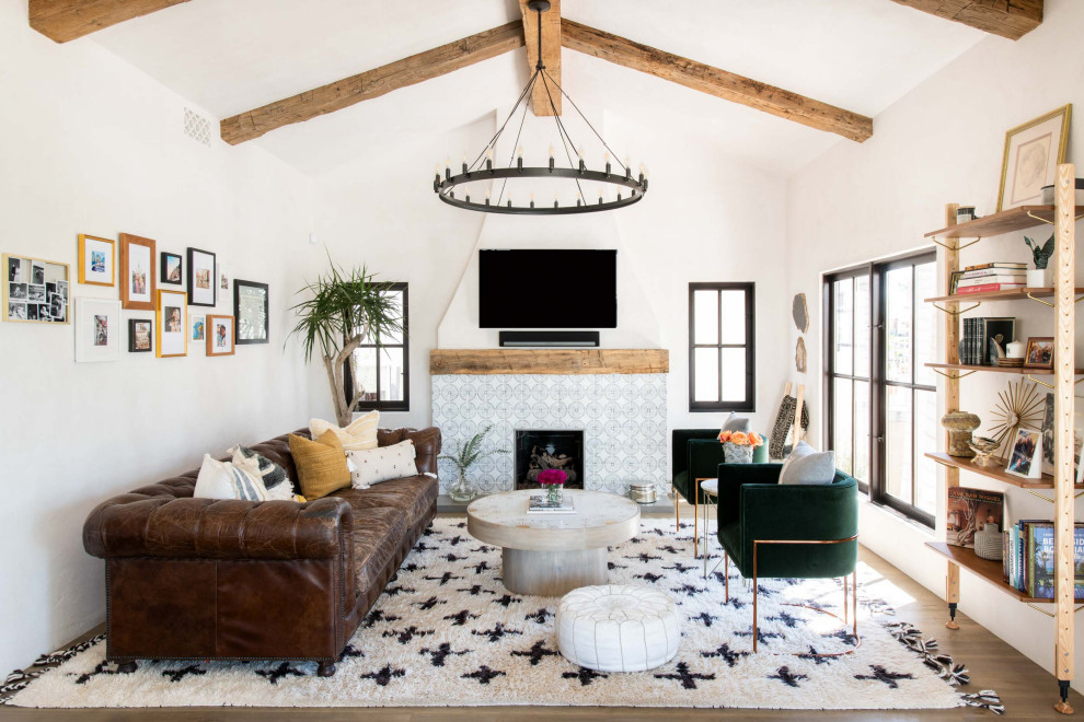 ロサンゼルスにある高級な中くらいな地中海スタイルのおしゃれなLDK (白い壁、無垢フローリング、標準型暖炉、タイルの暖炉まわり、壁掛け型テレビ、茶色い床、表し梁、三角天井) の写真
