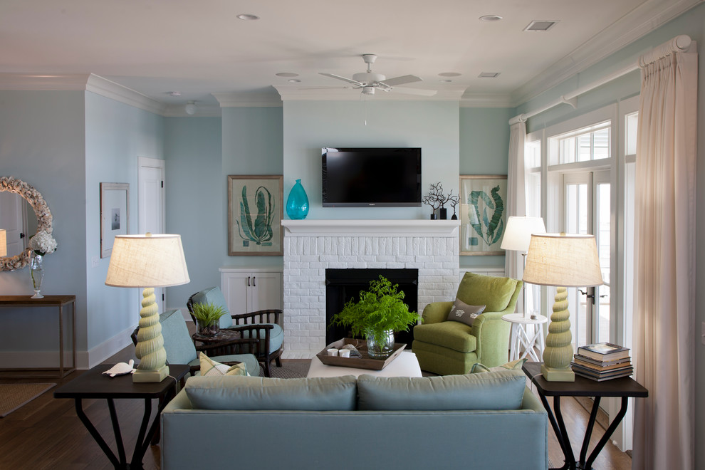 На фото: открытая гостиная комната среднего размера в морском стиле с синими стенами, темным паркетным полом, стандартным камином, фасадом камина из кирпича, телевизором на стене и красивыми шторами с