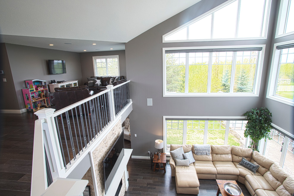 Geräumiges Klassisches Wohnzimmer im Loft-Stil mit grauer Wandfarbe, Tunnelkamin, Kaminumrandung aus Stein und TV-Wand in Edmonton